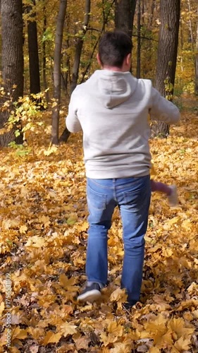 Father twirls daughter in circle while walking on leaf-covered ground. Fall colors fill scene, leaves crunch underfoot, creating a lively and cheerful environment in woods. Autumn fun with loved ones