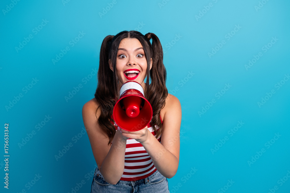 Fototapeta premium Energetic young woman holding a red megaphone in a vibrant pose against a blue background, expressing excitement and enthusiasm