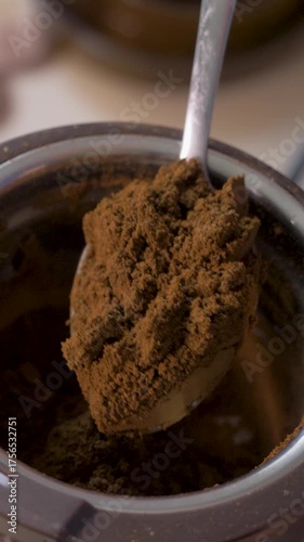 Spoon lifts fresh ground coffee from grinder. Strong aroma spreads. Powder prepared for energizing coffee moment. Roasted coffee beans have been ground down to be brewed for coffee