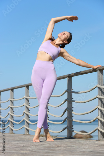 Fit woman stretching outdoors in lilac sportswear on boardwalk