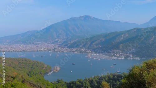 Time lapse: anchored yachts and gulets in Fethiye bay, some boats are gliding fast across the water against lush mountain and green hillsides backdrop. Marine tourism, timelapse and travel concept
