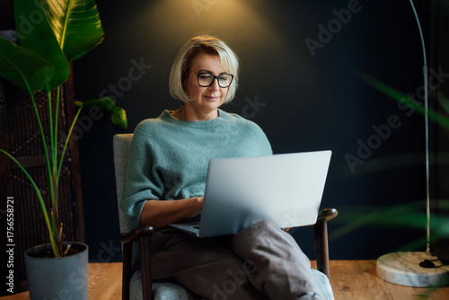 Relaxed 50's confident mature businesswoman in casual clothes, middle-aged experienced senior female professional working on laptop in cozy modern space. Female entrepreneur working remotely