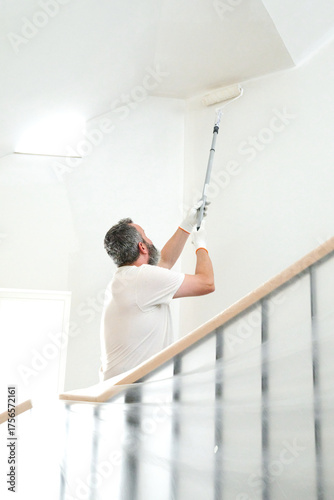 Painter on ladder rolling paint in bright stairwell