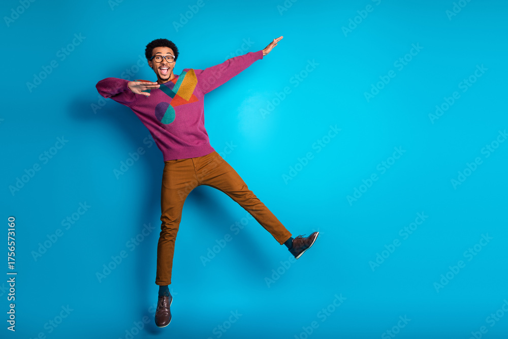 Obraz premium Trendy young man in vibrant sweater posing joyfully with unique style against bright blue background