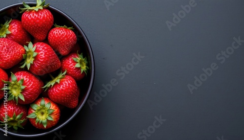 fresh ripe strawberries in a black bowl on the left side, set against a dark background, ideal for dessert, sweets, summer, vegan diet, or organic farm products