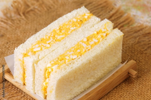 Traditional Japanese egg sandwich Tamago Sando with fluffy bread and creamy egg filling served on wooden plate.