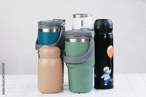 Variety of reusable tumblers in different designs and colors, arranged on white surface. Represents sustainability and modern lifestyle.