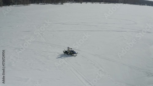 Aerial view from a drone following a woman riding a snowmobile across the expanses of a frozen snowy lake. Winter female extreme sports.