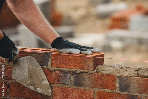 Bricklayer constructing stone wall using stone blocks, cement mortar mix and trowel