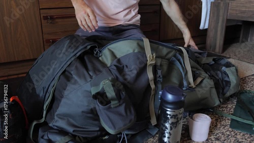 White man organizing hiking backpack on floor, steady hands clipping hydration bottle and adjusting shoulder straps while laying out small camping items nearby, quiet