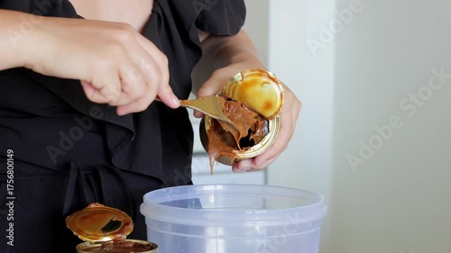 Spoonful of sticky caramel filling, Closeup of dessert ingredient being handled carefully, Person carefully scooping creamy caramel from jar into bowl during baking