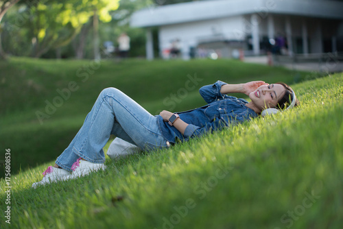 Slika na platnu Young Asian woman wearing headphones and jeans lie down and listen to music rela