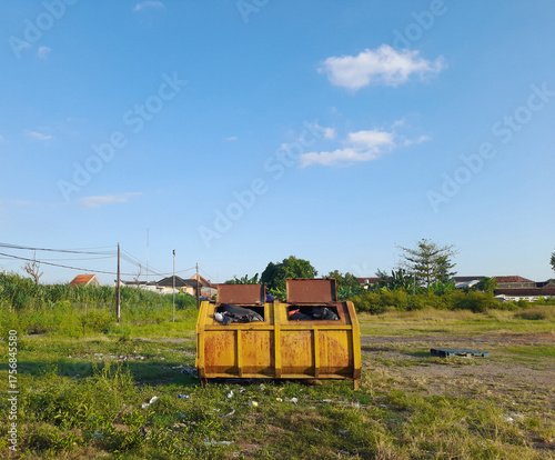 Yellow Dumpster Filled With Waste Materials in Open Field Under Bright Blue Sky