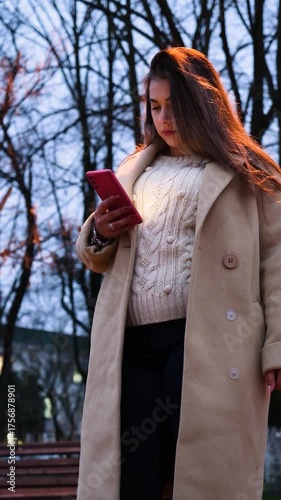 brunette woman wearing coat walking in the street at night using smartphone