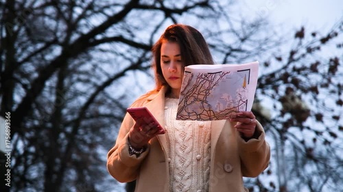 brunette woman wearing coat walking in the street at night using smartphone and map