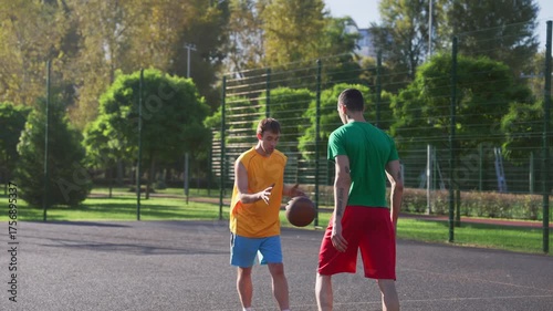 Athletic African American male basketball player receiving pass from teammate, driving to hoop and performing slam dunk with one hand while multiethnic sports teams playing streetball game on court