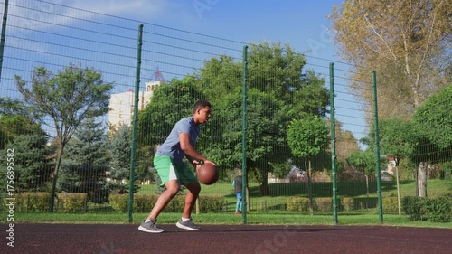Motivated athletic African American male basketball player jumping in the air, performing powerful slam dunk with one hand during sports training on outdoor court.