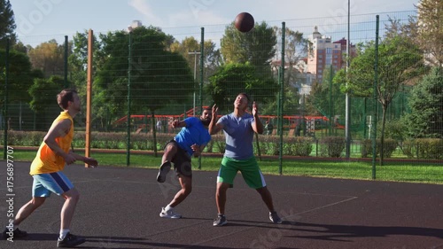 Active sporty fit multiracial basketball players playing two on two streetball game, passing ball and making forced turnovers on outdoor court.