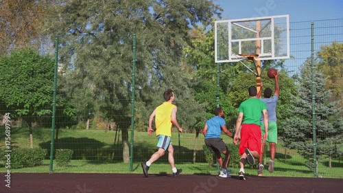 Skillful African American basketball player performing spin and drive motions, spinning around opposing defender and scoring points with layup while multiethnic athletes playing streetball on court.