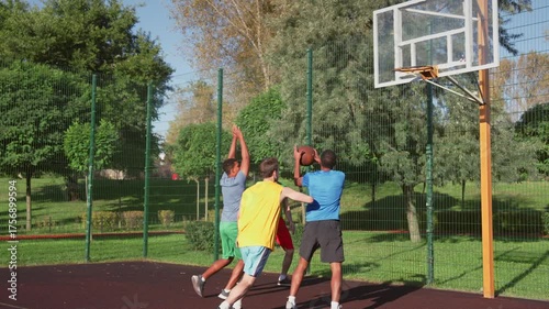 Excited sporty fit multiracial male basketball players scoring points with layup shot, celebrating win with chest bump and high five gesture while playing streetball game on outdoor court.