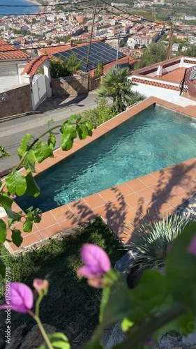Vertical aerial video of Beautiful view on Mediterranean sea bay in Spain, Blooming Bougainvillea. Luxury villa with swimming pool with clear blue water, tilled rooftops of white houses in beach town