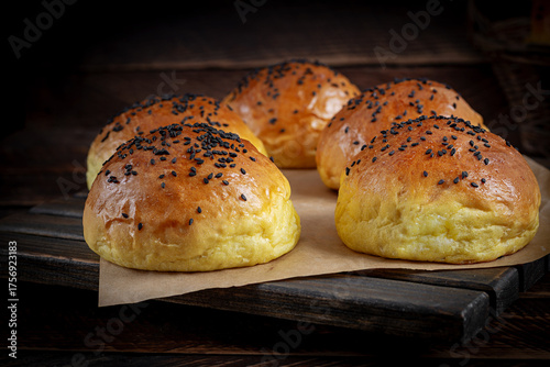 Homemade freshly baked plain golden brown soft hamburger buns topped with sesame seeds against wooden background. Homebaking, freshness, bbq concept