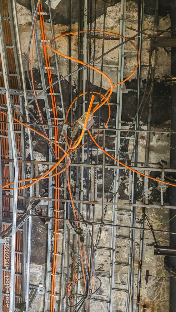 Fototapeta premium Utility lines and electrical cables secured to the ceiling of an industrial or office building. Installation of cable trays, electrical, and network cables during renovation or construction.