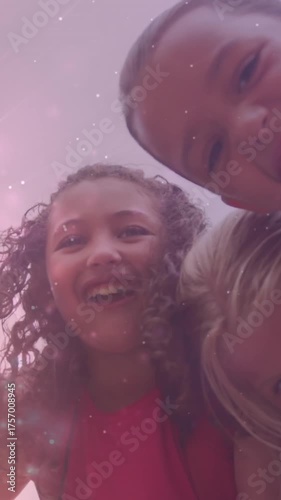 Animation of light particles over happy diverse schoolgirls embracing outdoors