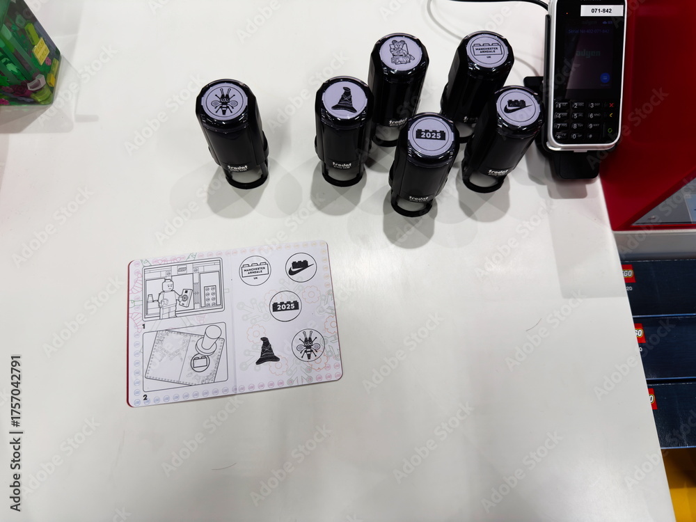 Naklejka premium Five black stampers and a payment terminal sit beside an Lego instruction sheet on a white desk