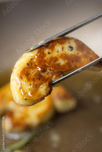 Obraz na płótnie Chef's Tongs Lifting a Perfectly Seared, Golden-Crusted Foie Gras Slice from the