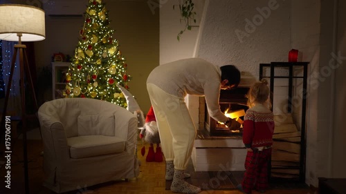 Grandmother lighting a fireplace with her grandson near a Christmas tree. Cozy holiday evening filled with warm light, family love, and festive winter spirit at home.