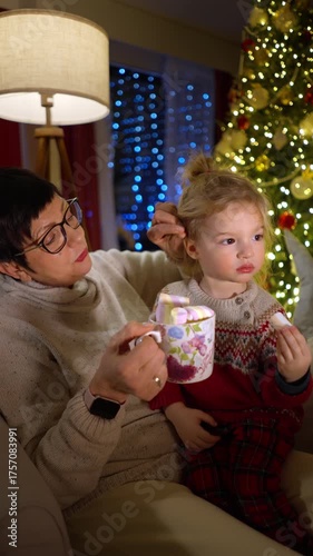Grandmother tells Christmas stories to her grandson by the fireplace. Warm light, festive tree, and cozy winter night create a magical family moment full of love, peace, and holiday spirit.