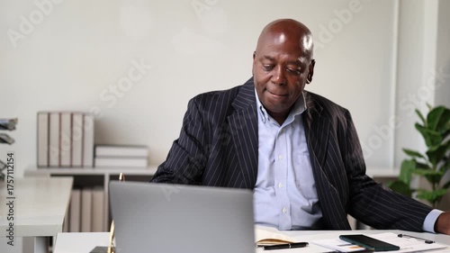 Mature African American businessman sitting at his desk in a modern office, ending a phone call, and then opening his notebook to review his schedule and take some notes for work