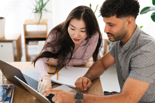 A man and a woman collaborate on a project, pointing at a laptop screen and taking notes in a notebook.