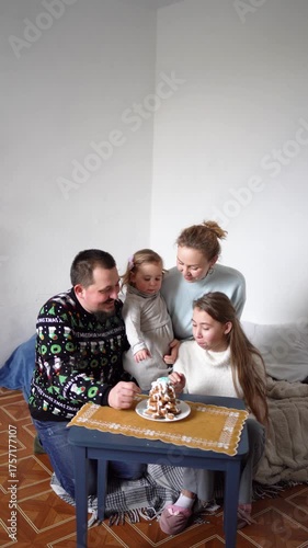     family with daughters toddler and teenager make a Christmas tree from gingerbread cookies and decorate it with white cream and blue sugar snowflakes