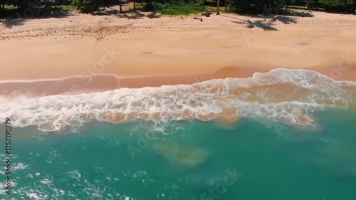 Beautiful aerial footage of turquoise ocean waves rolling onto a golden sandy beach under clear sky. Perfect for travel, relaxation, or summer themes.