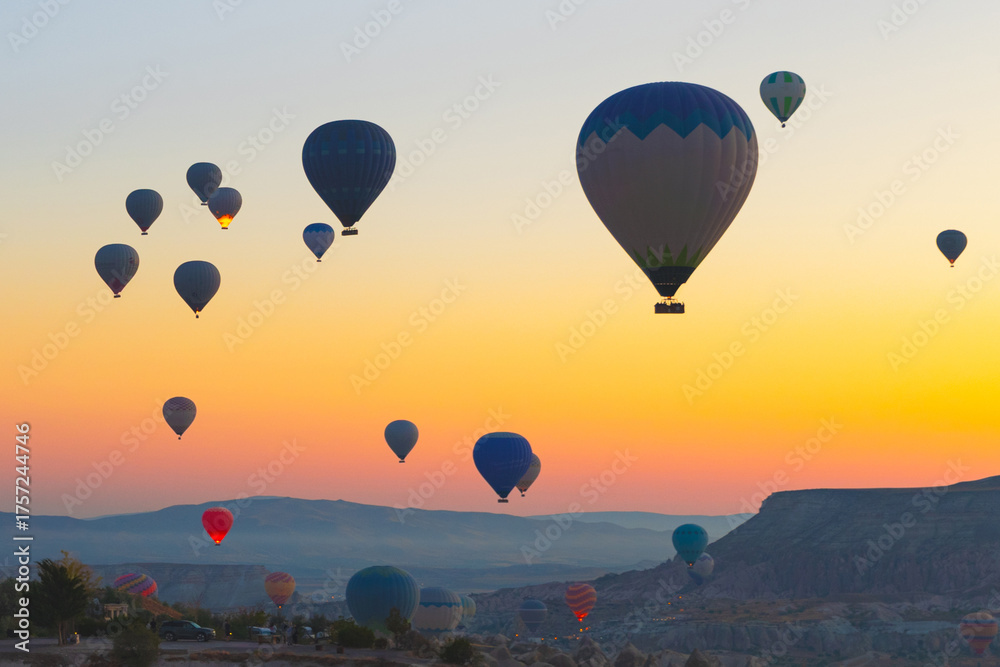 Naklejka premium Hot air balloons float over the valleys of Cappadocia at sunrise, creating a colorful view above the rocky landscape.