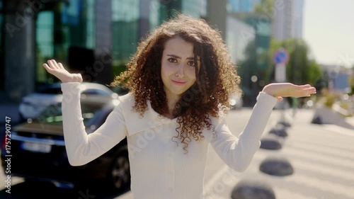 Confused curly haired woman shrugging outdoors on sunny city street