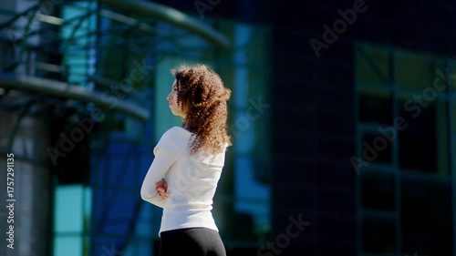Curly haired young woman standing with arms crossed in urban city scene