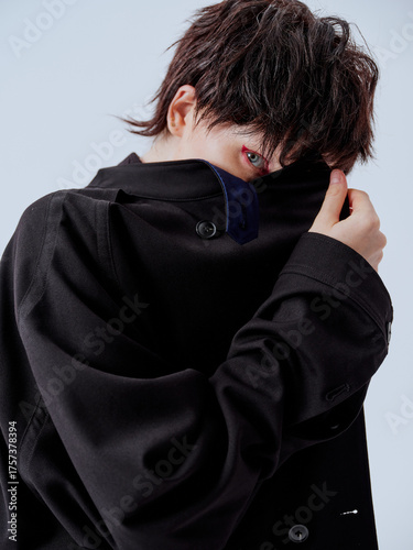 Mysterious woman in black coat covering face, modern portrait shot conveying intrigue.