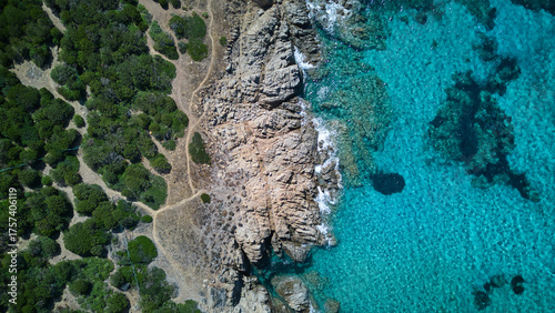 Beautiful drone shot of the Sardinian seaside, blue of the sea, green of the forest and the rocky beach in between