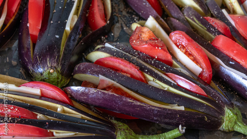Background of sliced vegetables. Sliced eggplant and tomatoes on a platter are being prepared for baking in the oven. Fresh vegetables are sprinkled with pepper.