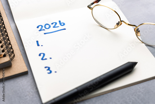 Open notebook with handwritten 2026 and numbered list beside pen and eyeglasses symbolizing new year goals planning resolution and personal vision