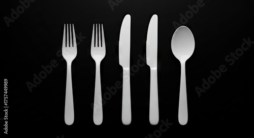 Two forks two knives and one spoon are arranged in a straight line on a black background