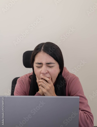 Foto A young woman sits at her office desk, looking bored and disengaged while staring at her laptop screen, experiencing a lack of motivation during a quiet workday in a modern office