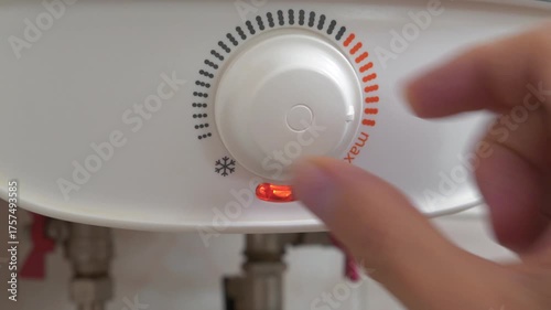 Regulator for heating cold water in boiler. Man turns temperature control on heater. Red light indicator comes on, boiler has turned on to heat water. Boiler heats water from cold water supply system