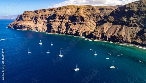 Aerial view of coastal cliffs, blue ocean, and sailboats on sunny day