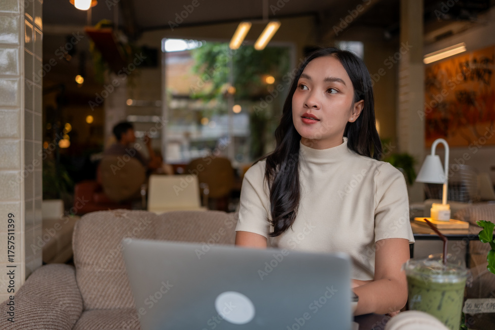 Fototapeta premium Thoughtful Asian woman using laptop working in cafe