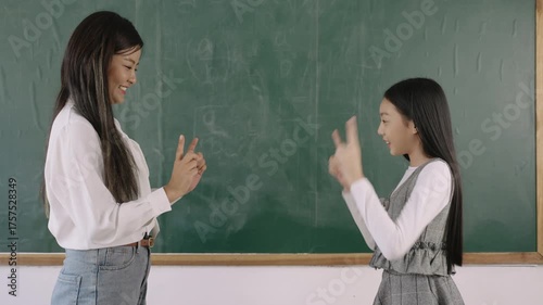 Back to school concept. Happy young Asian female teacher and her girl student relax by standing and playing a game of rock, paper, scissors together having fun and enjoying in the front classroom. 