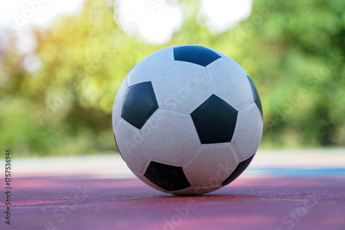 A black and white soccer ball sits alone on a red and purple outdoor court with a blurred green background.